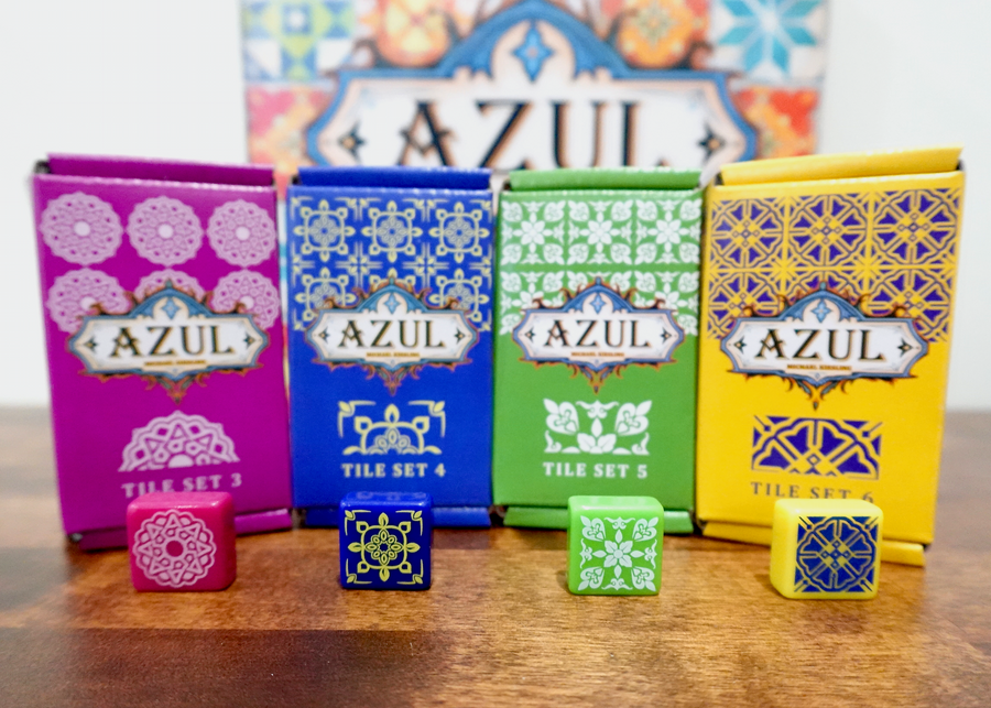 A photo of the 3rd, 4th, 5th, and 6th tile sets for use with the board game Azul. The four boxes are sitting in front of the game box and have one example tile sitting in front of the tile set boxes.