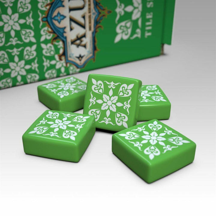 A photo of the fifth tile set for use with the board game Azul. These square tiles are green with a white pattern printed on one side. A pile of tiles is sitting on a white background with the box partially visible in the back.