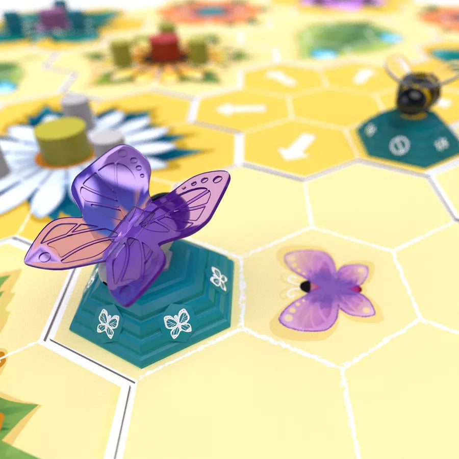 A photo of the plastic purple butterfly token from the mini-expansion Fly, Butterfly! for use with the board game Beez. The butterfly token is attached to a hexagon base and is sitting on a hexagon-tiled game board.
