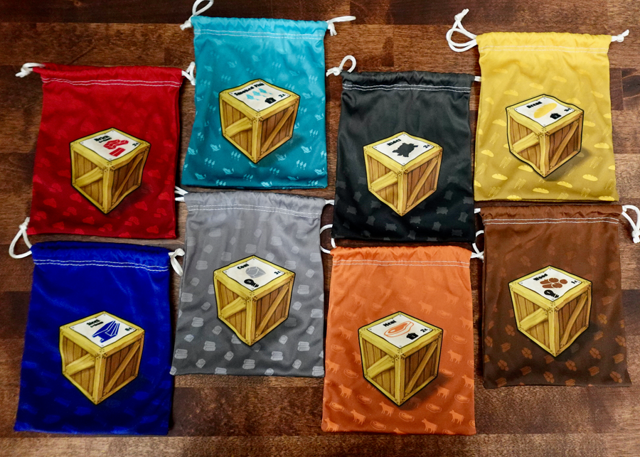 A set of microfiber drawstring bags for use with the board game Le Havre, each with different colored background and a single crate pictured in the middle.