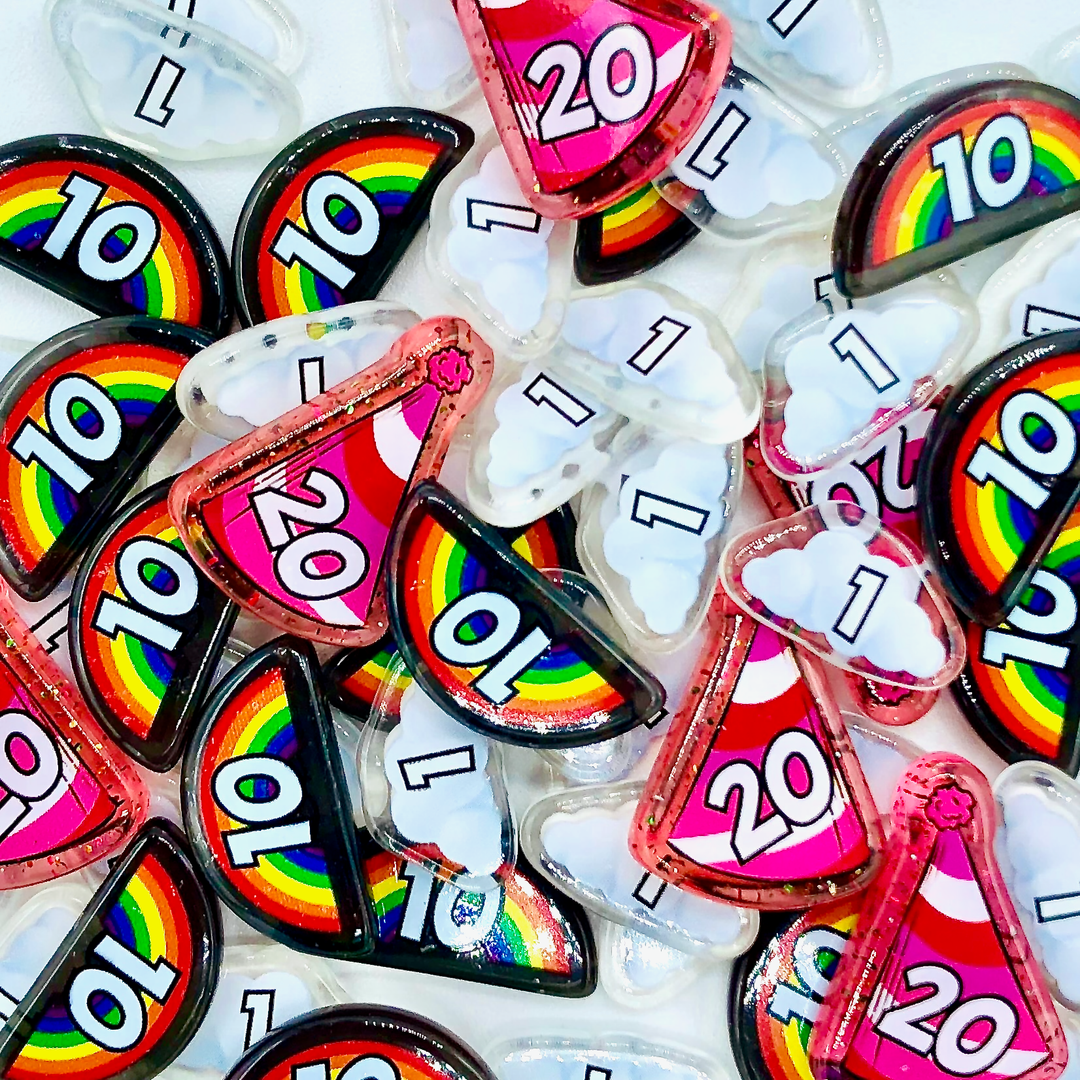 A pile of plastic tokens for use with the card game L.A.M.A., featuring bits in the shapes of clouds, rainbows, and party hats, with the numbers 1, 10, and 20 printed on them.