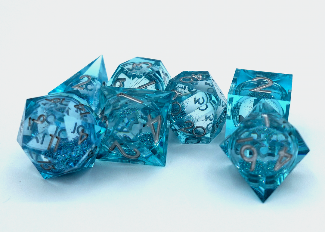 A pile of seven dice on a white background, each one a different shape, made from transparent plastic that is different shades of aqua, and contains a circular cavity in the middle filled with glitter and liquid.
