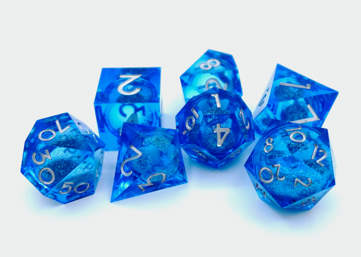A pile of seven dice on a white background, each one a different shape, made from transparent plastic that is different shades of blue, and contains a circular cavity in the middle filled with glitter and liquid.