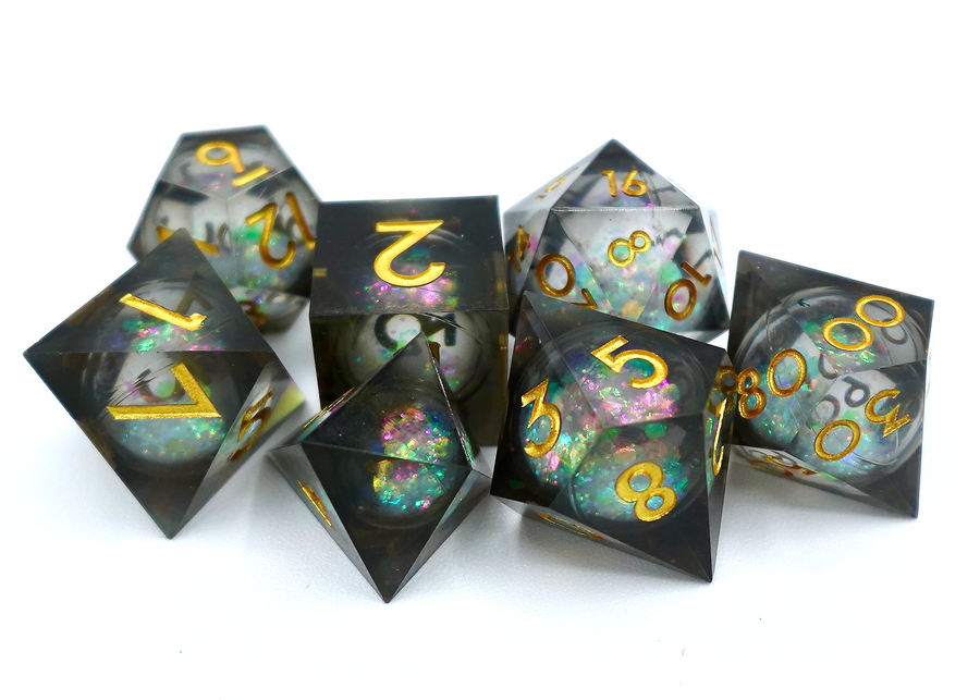 A pile of seven dice on a white background, each one a different shape, made from transparent plastic that is black and mixed pastel colors, and contains a circular cavity in the middle filled with glitter and liquid.