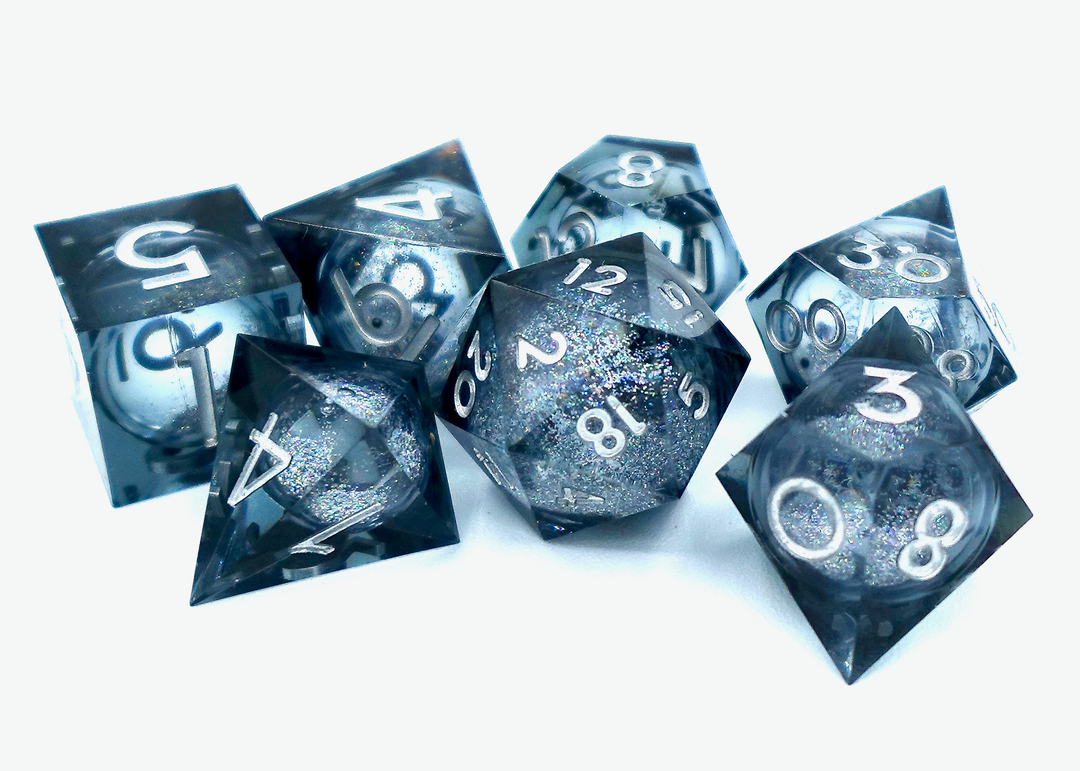 A pile of seven dice on a white background, each one a different shape, made from transparent plastic that is black and gray, and contains a circular cavity in the middle filled with glitter and liquid.