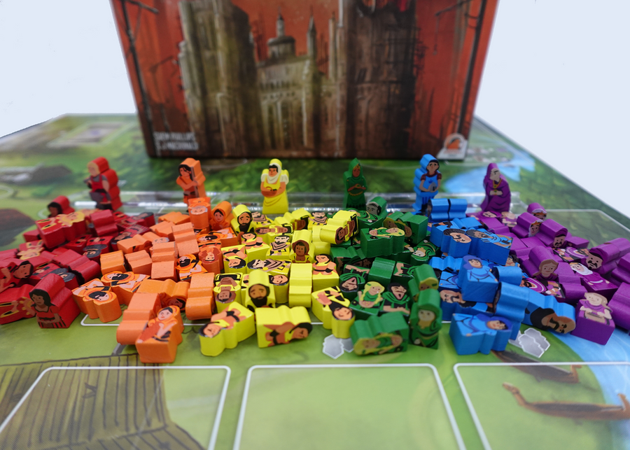 A photo of a pile of people tokens made from wood, for use with, and sitting in front of, the board game Architects of the West Kingdom. These tokens are painted different colors, and each has its own shape, clothes, hair, and expressions painted on one side.