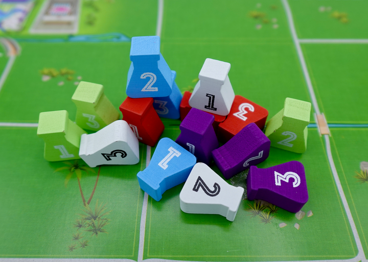 A close up photos of wooden tokens for use with the board game Dinosaur Island. The tokens are shaped like glass beakers, are painting a variety of colors, have the numbers 1, 2, or 3 printed on them, and are sitting on one of the player game boards.