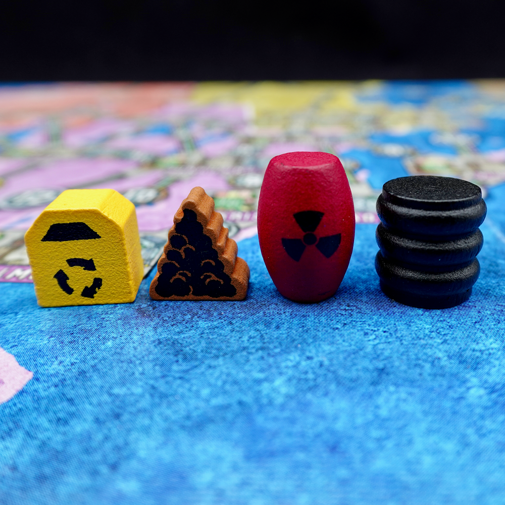 A close up photo of a single example of each wooden upgraded tokens for the board game Power Grid, made by Meeple Source, specifically a yellow recycling bin, a brown pile of trash, a black oil barrel, and a red nuclear canister.