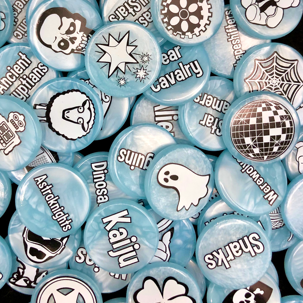 A photo of upgrades for the card game Smash Up, featuring a pile of light blue, plastic tokens with either a word or simple black and white illustration printed on each side.
