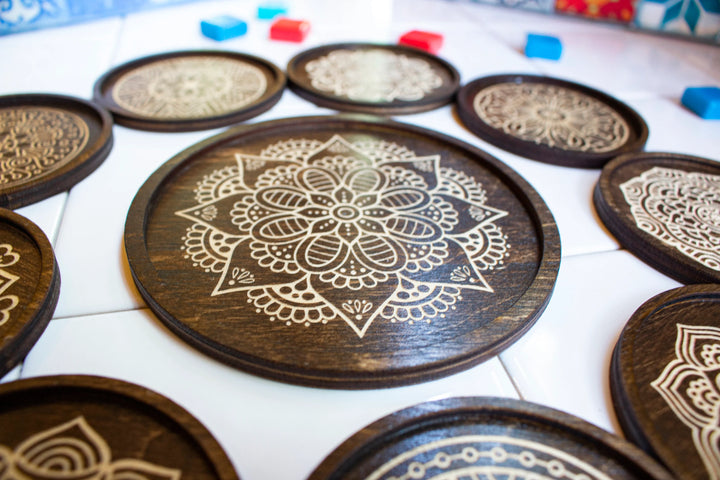 An overhead shot of a set of wooden tile holders for use with the board game Azul, created by Strata Strike, featuring a carved mancala in the center of each wooden circle.