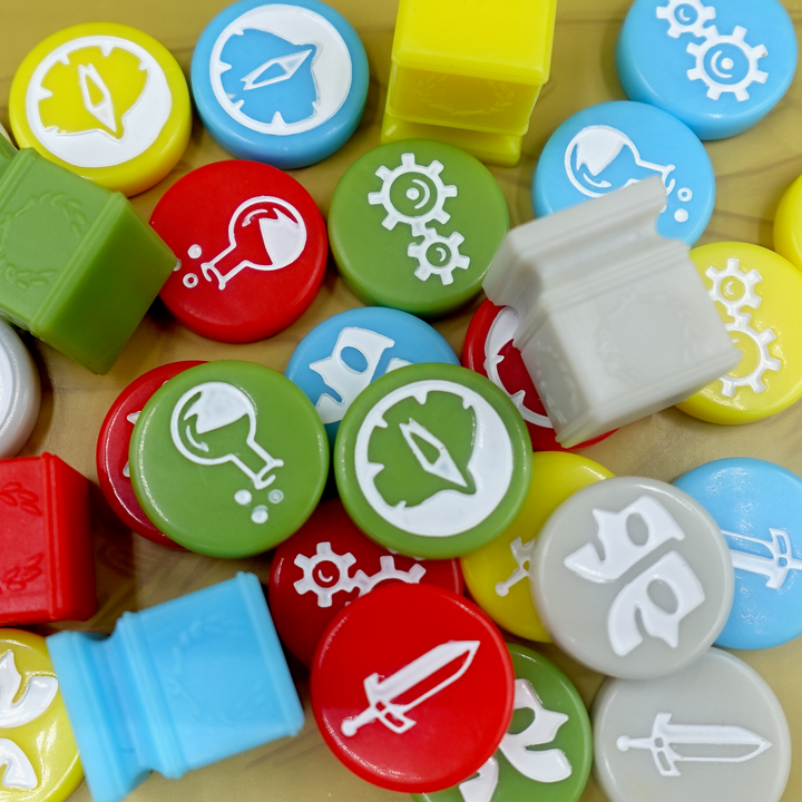 An overhead photo of a jumble of GeekUp bits for use with the board game Tapestry. Most bits are circular disks in a variety of colors, each with an engraved symbol in the center. The rest of the tokens are square, plastic columns with a laurel wreath printed on each side.