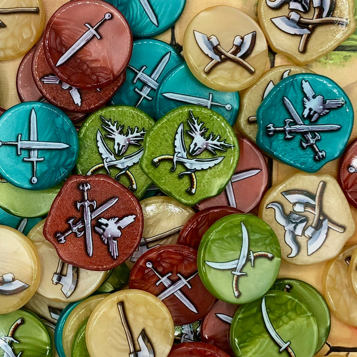 A photo of plastic tokens for use with the board game Tash-Kalar in a variety of colors, all with weapons of different types printed on the tops and bottoms.