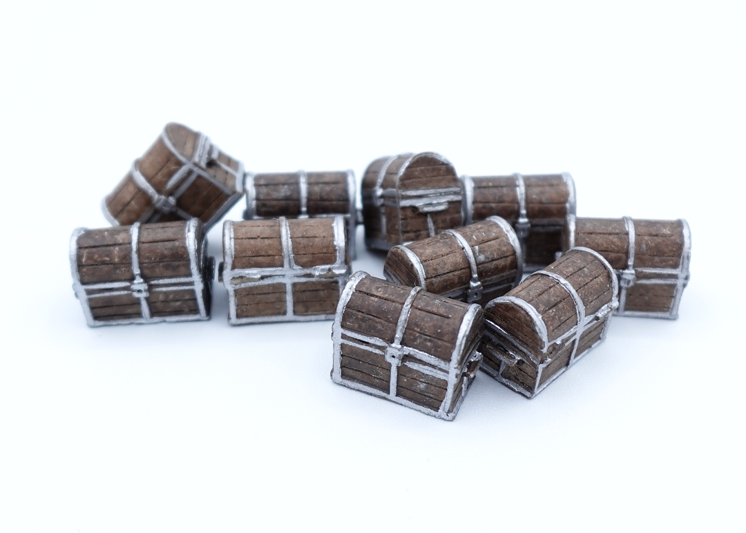 A close up photo of a group of tokens shaped and painted to look like a metal and wooden treasure chests, sitting on a white background.