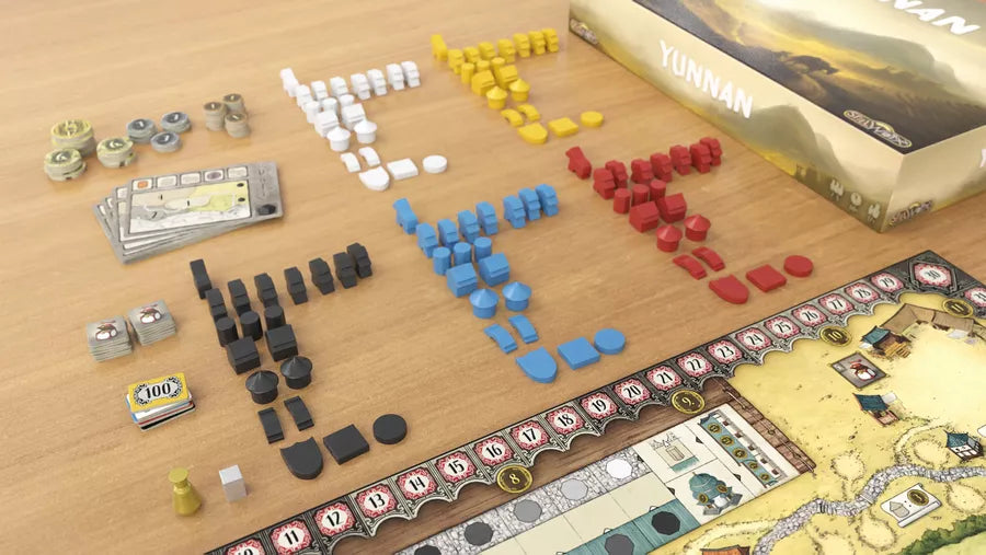 A photo of some components from the board game Yunnan. Pictured are part of the game box, part of the game board, all of the wooden pieces included in the game sorted by color, a pile of cards, and various piles of cardboard tokens and money.