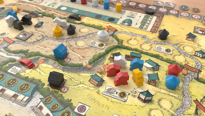 A photo of some components from the board game Yunnan. Pictured are a close-up of the game board with wooden tokens shaped like people and houses placed on an overhead map.