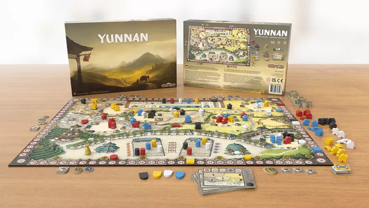 A picture of the board game Yunnan, with the entire game and all of its components laid out in front of both the box lid and box bottom, and all of on wooden tabletop.