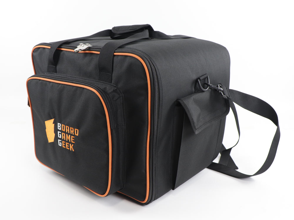 An angled front view of a black carry bag and backpack with orange trim, and an embroidered logo on the front pocket that reads "BoardGameGeek". The bag has handles on the top and a shoulder strap draped in the back.