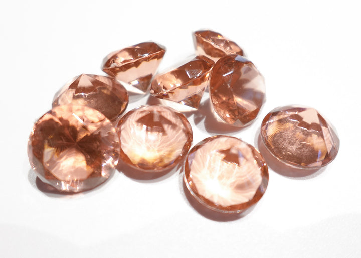 A photo of 10 rose colored, transparent plastic gems on a white background.