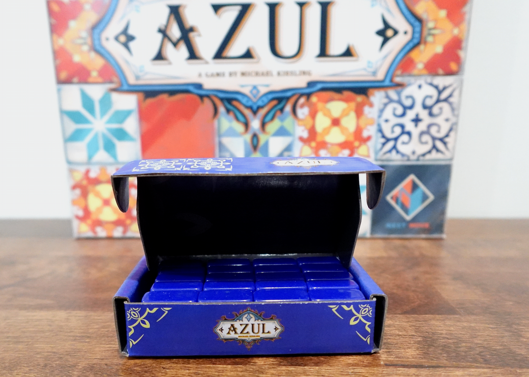 A photo of the fourth tile set for use with the board game Azul. These dark blue tiles are sitting in a matching dark blue box, which in turn is sitting in front of the game box of Azul.