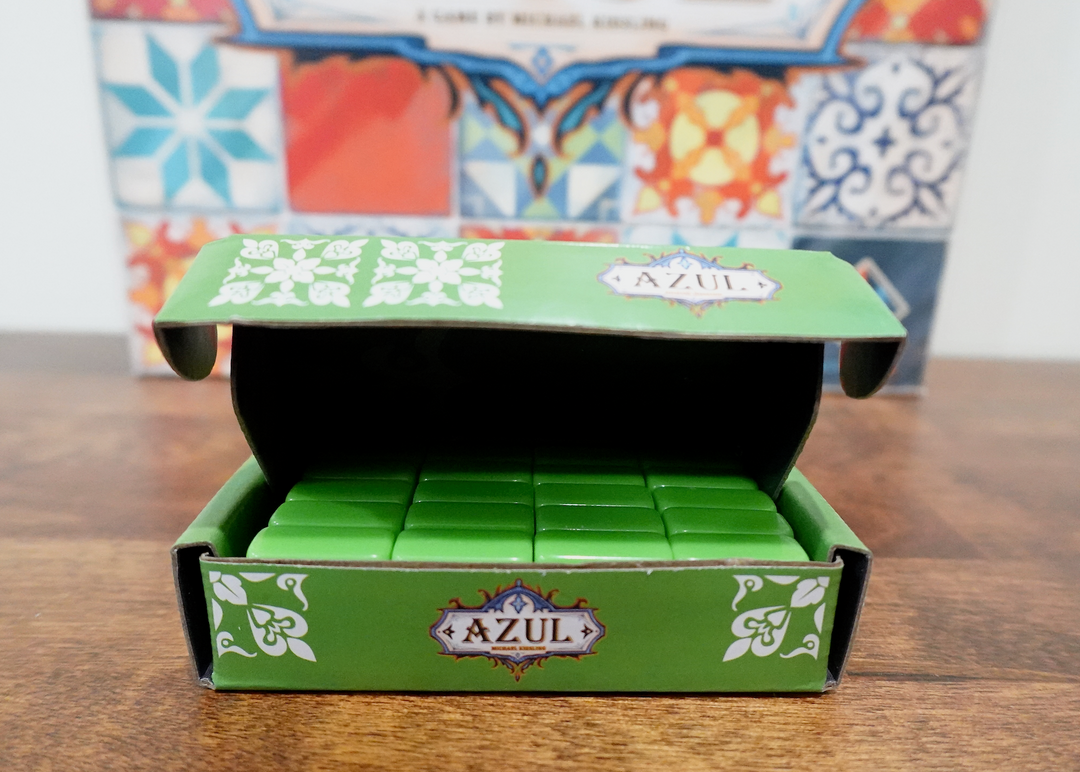 A photo of the fifth tile set for use with the board game Azul. These green tiles are sitting in a matching green box, which in turn is sitting in front of the game box of Azul.