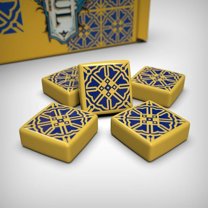 A photo of the sixth tile set for use with the board game Azul. These square tiles are yellow with a dark blue pattern printed on one side. A pile of tiles is sitting on a white background with the box partially visible in the back.