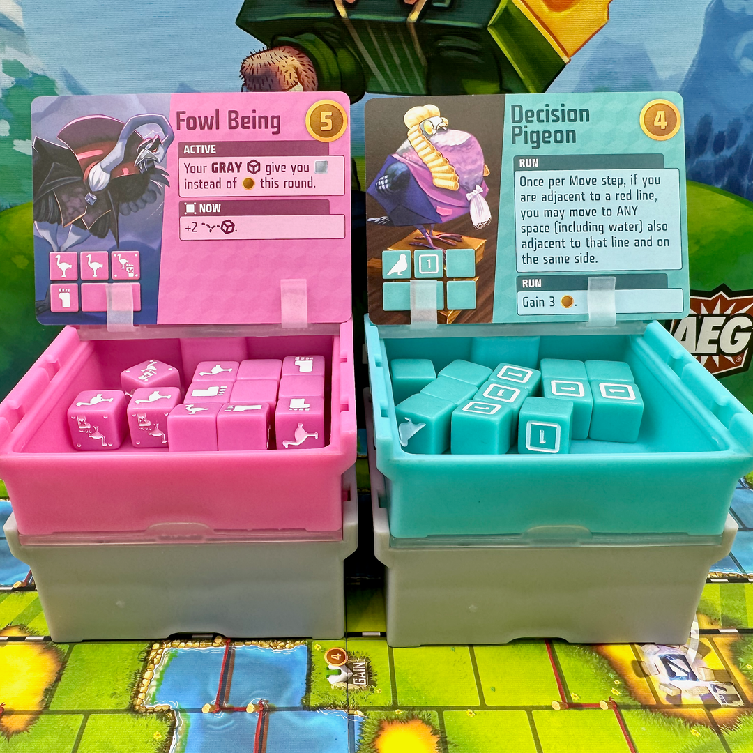 A photo of four, plastic storage boxes for use with the board game Cubitos. Each box has a clear top with dice of a matching color inside. One box is pink, one teal, and two gray. The pink and teal boxes are sitting on top of the gray boxes and have their lids flipped open. A card from the game is resting on each lid. The boxes are sitting on the game board from Cubitos and part of the image of the game box cover is visible in the background.