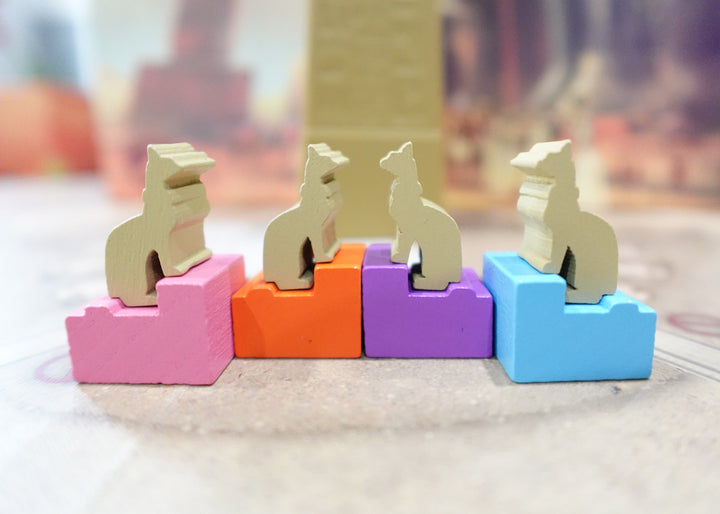 A closeup photo of wooden, cat-shaped tokens sitting on top of colorful wooden buildings.
