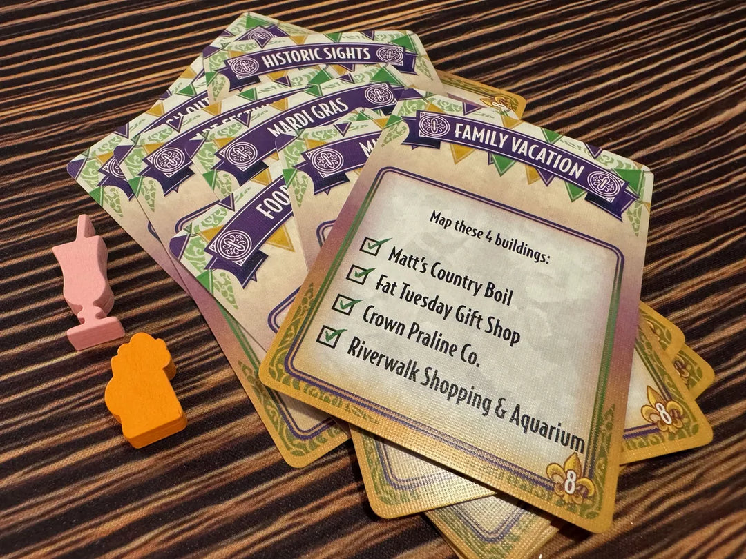 A photo of the mini expansion Tourism Expansion for the board game French Quarter. The photo features a pile of cards with text in English, and two wooden tokens: both in the shapes of fancy alcoholic drinks.