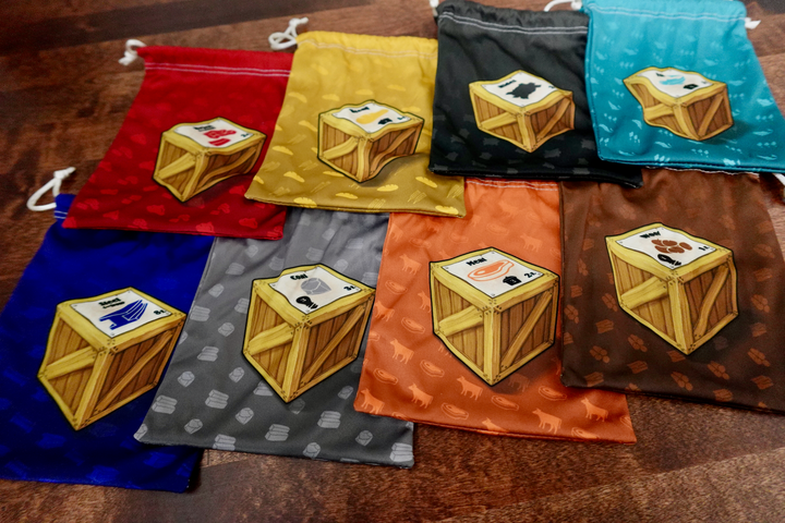 A set of microfiber drawstring bags for use with the board game Le Havre, each with different colored background and a single crate pictured in the middle.
