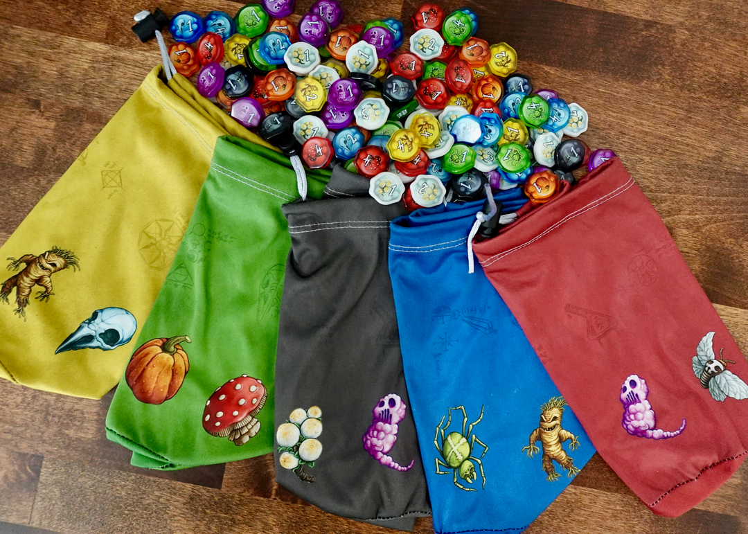 A set of microfiber drawstring bags for use with the board game Quacks of Quedlinburg, each with different colored background and potion ingredient symbols along the bottom, like a pumpkin, mushroom, spider, mandrake, and moth.  Above these bags are a pile of plastic upgraded tokens for use with the same game.