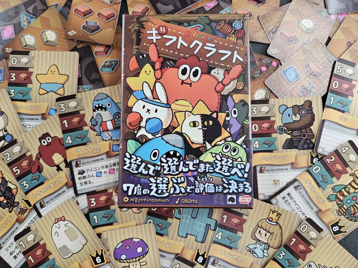 The box for the board game Gift Craft, sitting on top of a pile of cards from the game. Both the game box and cards feature cartoon illustrations of plushie characters, with text in Japanese.