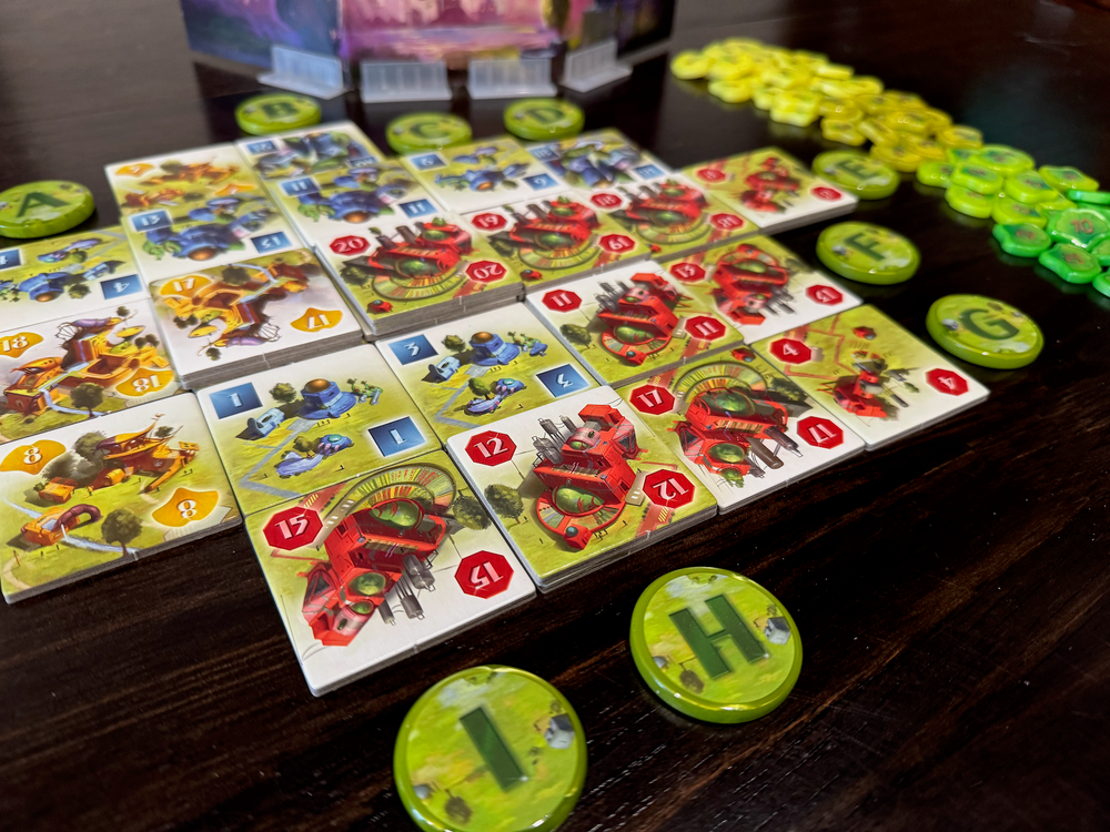 A photo of tiles from the board game Ginkgopolis, surrounded by upgraded, circular tokens, each printed with a single letter in the center. In the background is a player shield and upgraded tokens for the victory point pieces from the same game.