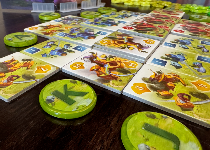 A photo of tiles from the board game Ginkgopolis, surrounded by upgraded, circular tokens, each printed with a single letter in the center. In the background is a player shield and upgraded tokens for the victory point pieces from the same game.