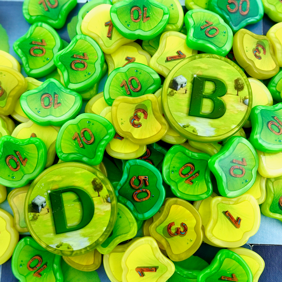 A photo of a jumble of GeekUp tokens for use with the board game Ginkgopolis. Some of the tokens are in the shape of a Ginko leaf and have a single number printed in the center. The other bits are larger, circular, and have a single letter printed in the center.