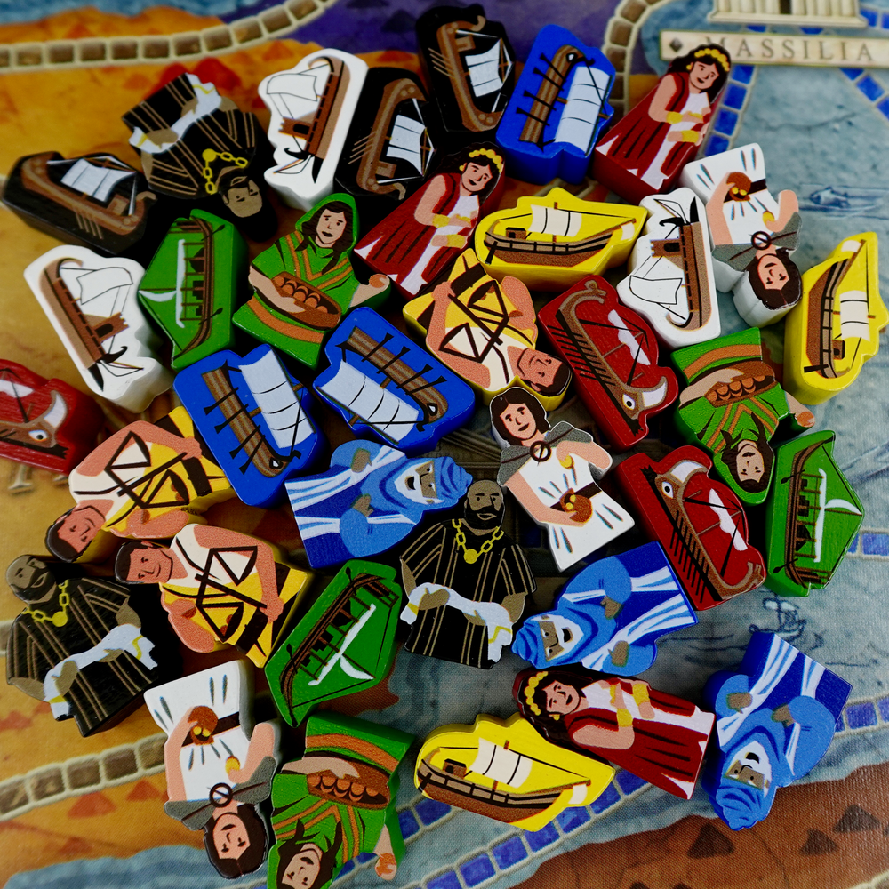 A pile of wooden tokens for use with the board game Concordia, featuring people with ancient Green clothing and boats of the same time period, in a variety of painted colors