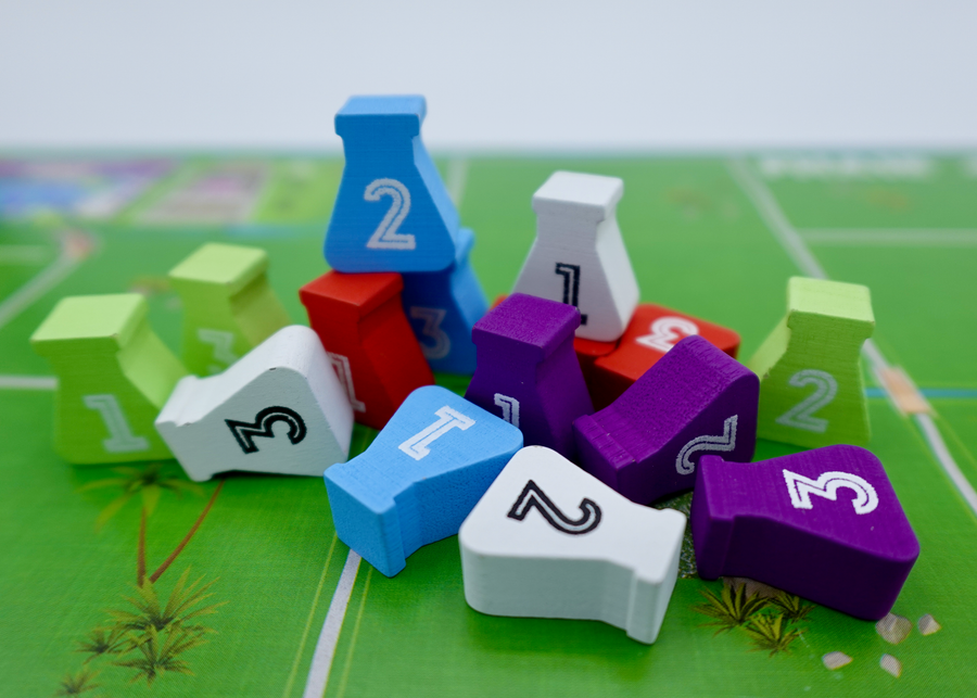 A close up photos of wooden tokens for use with the board game Dinosaur Island. The tokens are shaped like glass beakers, are painting a variety of colors, have the numbers 1, 2, or 3 printed on them, and are sitting on one of the player game boards.