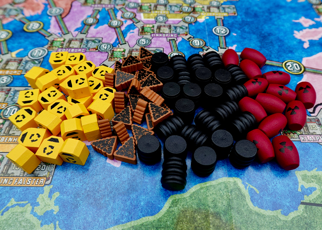 A photo of wooden upgraded tokens for the board game Power Grid, made by Meeple Source, specifically yellow recycling bins, brown piles of trash, black oil barrels, and red nuclear canisters.