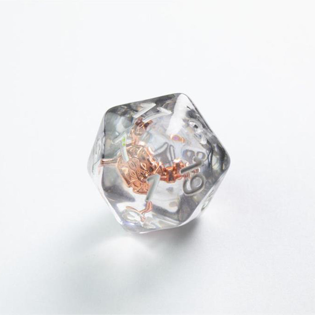 A close up photo of a single, clear, transparent, 20-sided die, with a copper token embedded in the center.