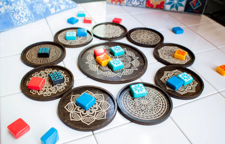 An overhead shot of a set of wooden tile holders for use with the board game Azul, created by Strata Strike, featuring a carved mancala in the center of each wooden circle and with the original game pieces sitting on top of each circle..