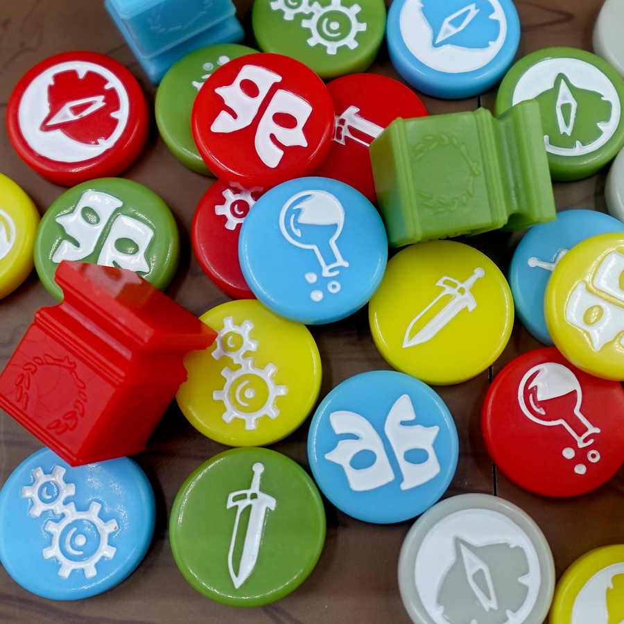 An overhead photo of a jumble of GeekUp bits for use with the board game Tapestry. Most bits are circular disks in a variety of colors, each with an engraved symbol in the center. The rest of the tokens are square, plastic columns with a laurel wreath printed on each side.