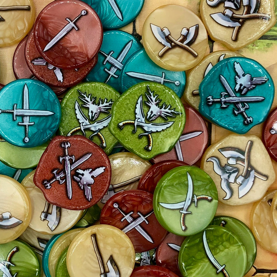 A photo of plastic tokens for use with the board game Tash-Kalar in a variety of colors, all with weapons of different types printed on the tops and bottoms.