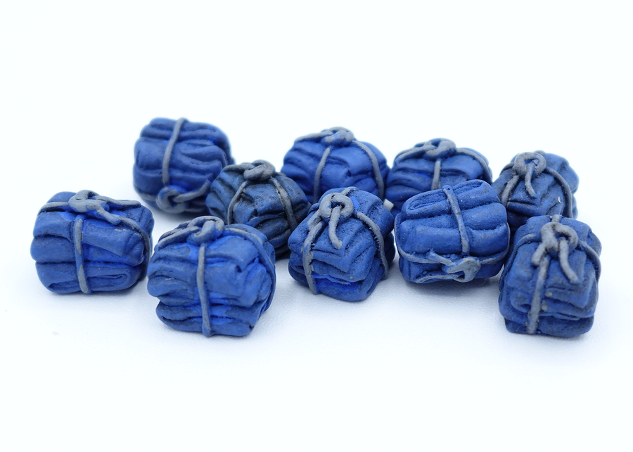 A close up photo of a group of tokens shaped and painted to look like tied bundles of blue cloth, sitting on a white background.