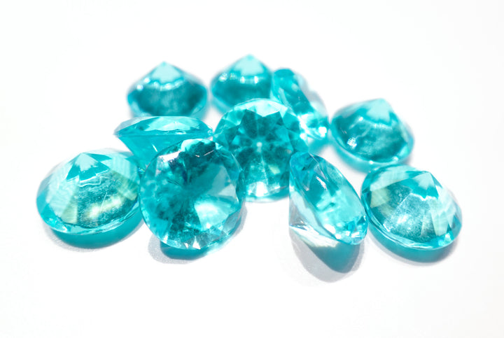 A photo of 10 cyan, transparent plastic gems on a white background.