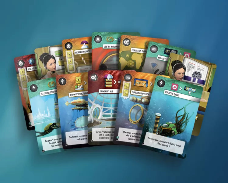 A photo of 12 cards for use with the board game Underwater Cities. Each card has a colored top with a title and symbols, an illustration in the middle, and text describing the card's abilities in the game at the bottom.