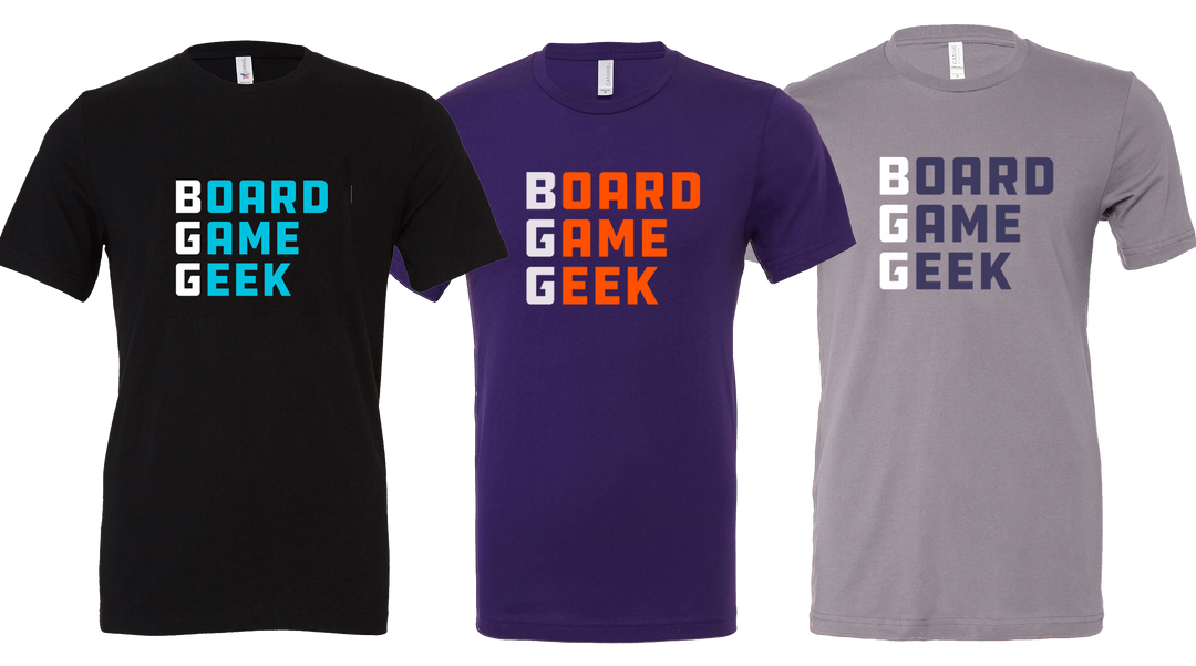 A photo of three different t-shirts, each with identical words of BoardGameGeek printed on the front, in three different color combinations: black with aqua letters, purple with orange letters, and gray with purple letters.