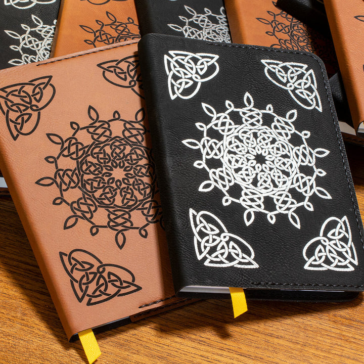 A group of leather journals: half are brown leather with a black Celtic pattern and the others are black leather with a white Celtic pattern.