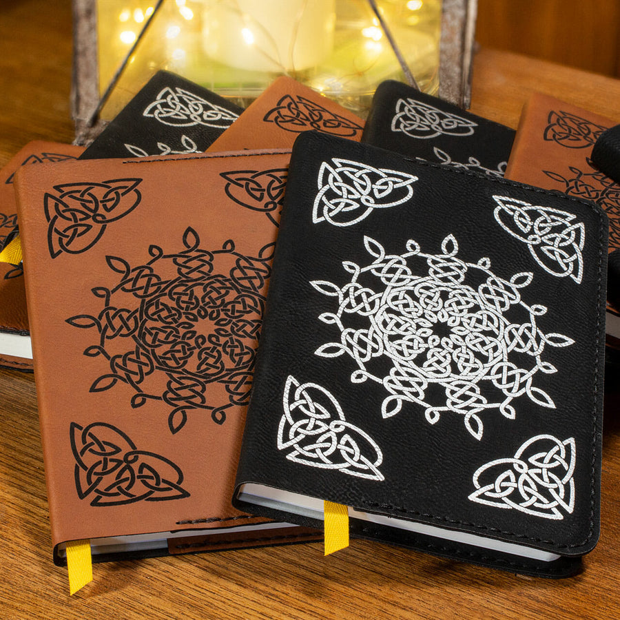 A group of leather journals: half are brown leather with a black Celtic pattern and the others are black leather with a white Celtic pattern.