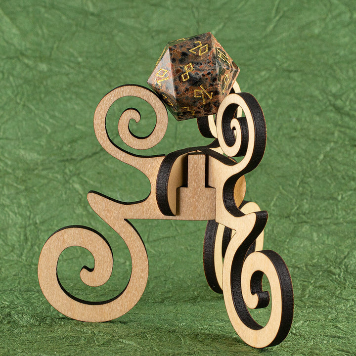A laser-cut wooden, tripod stand with decorative curves, holding up a 20-sided die, on a green background
