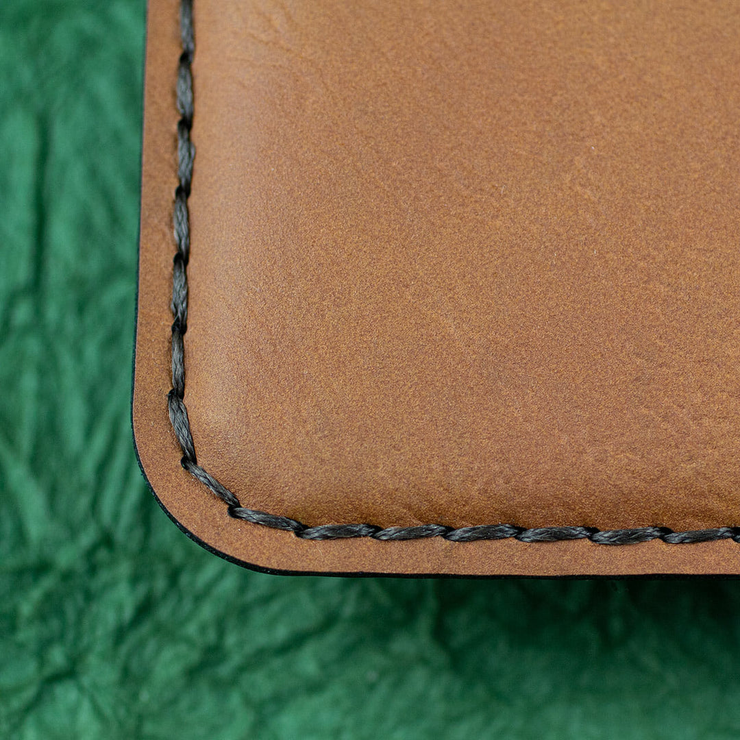 A close-up photo of black stitching around the edge of a brown leather journal cover.