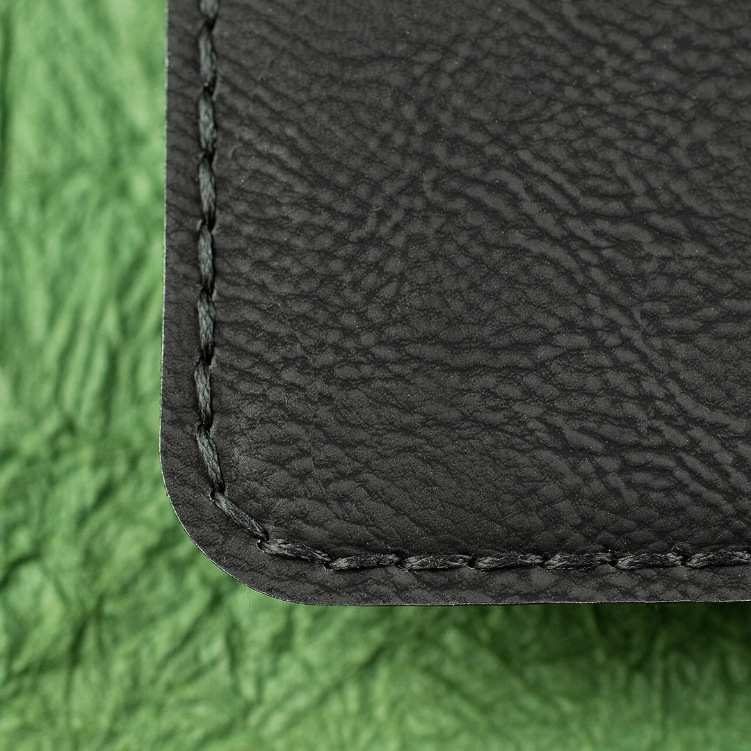 A close-up photo of black stitching around the edge of a black leather journal cover.
